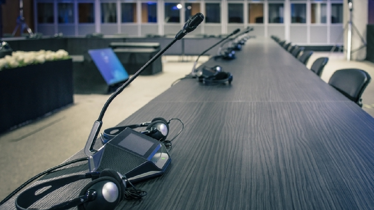 Mikrofone für die Verdolmetschung, die auf einem langen Konferenztisch aufgestellt sind